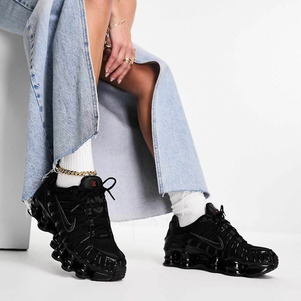 Woman wearing black Nike Shox TL sneakers with denim skirt