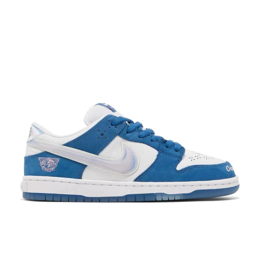 Nike SB Dunk Low "Born x Raised" sneaker side view showing white leather, blue nubuck, iridescent Swoosh, and unique heel embroidery | Collaboration SB Dunks